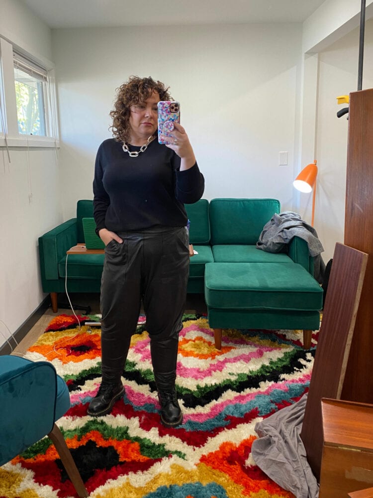 Alison wearing a black merino wool crewneck from Universal Standard with black faux leather joggers from Spanx. She has black platform Doc Marten boots on her feet and a very thick silver link necklace from Jenny Bird.