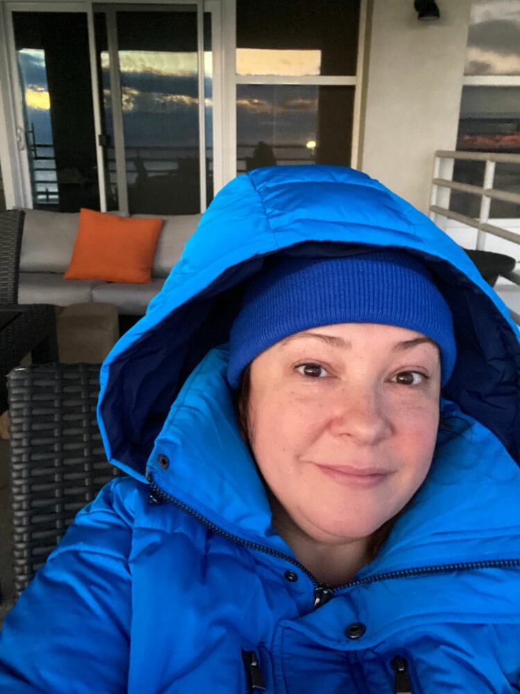 Alison sitting on a balcony in a blue puffer coat and beanie