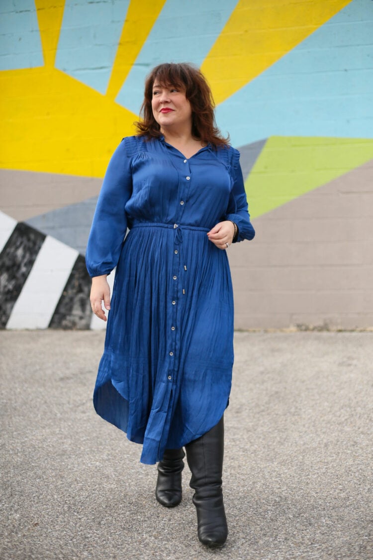 Alison in a blue silky shirtdress from chicos. She is walking towards the camera looking to the right.