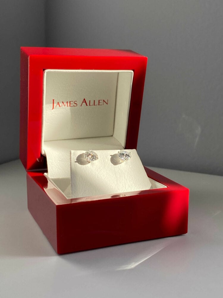 A pair of James Allen diamond stud earrings in one of the company's signature red lacquer boxes