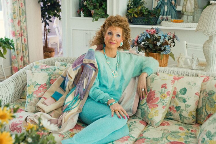 Jessica Chastain as Tammy Faye Bakker, wearing a turquoise knit jogging suit sitting on a floral couch.