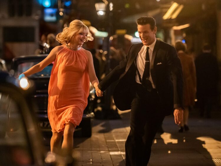 Photo of actors Anya Taylor Joy and Matt Smith in the movie Last Night in Soho. They are running down the street holding hands and laughing.