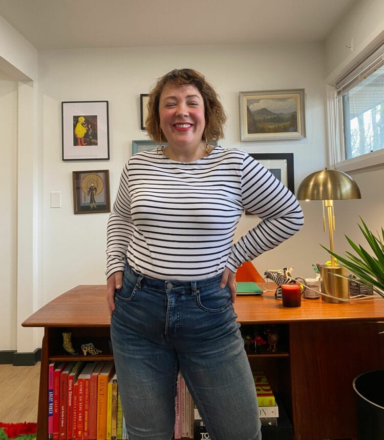 Alison of Wardrobe Oxygen wearing a white with black striped long sleeve Breton t-shirt tucked into a pair of jeans. Her hand is on her hip and she is smiling at the camera