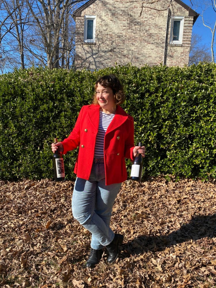 My Favorite Breton Shirt is Under $35 1 Alison of Wardrobe Oxygen wearing her favorite Breton top under a red wool peacoat. She is standing outside, holding two bottles of wine and smiling at the camera