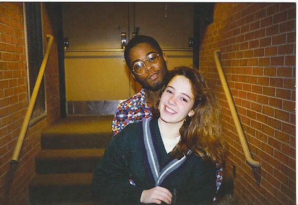 two high school students hugging in a school auditorium. The woman is wearing a dark green v-neck sweater from Gap