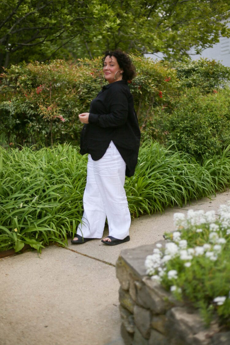 Universal Standard Dawn tunic over a pair of white linen wide leg pants. On her feet are Birkenstock sandals.