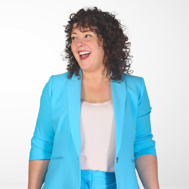 Alison Gary, the editor in chief and owner of Wardrobe Oxygen, a style blog for women over 40. Alison is wearing a turquoise pantsuit with an ivory shell underneath. She has curly brown shoulder length hear, she is laughing and looking to her right.