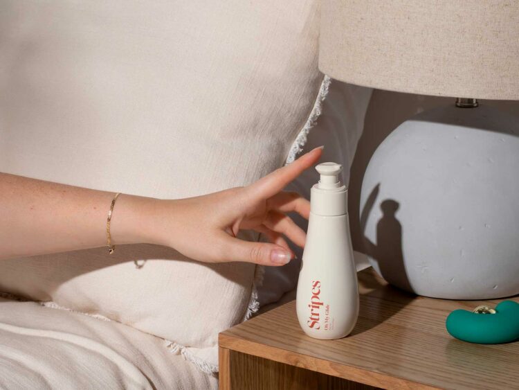 Image of a bottle of product from the brand Stripes on a bedside table, a hand reaching from the bed to grab the bottle