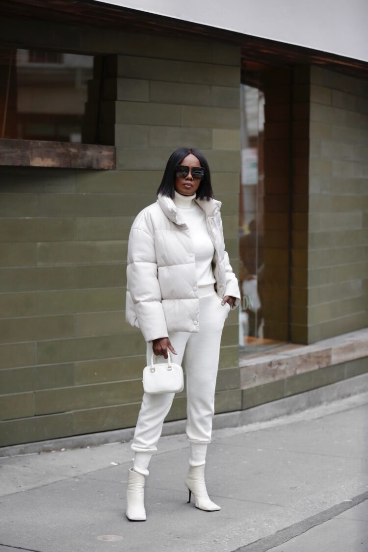 Image of over 50 influencer Elaine Davis AKA @squarepearls. She is wearing an all white winter look with a puffer jacket, slim joggers, and heeled white ankle booties with square toes.