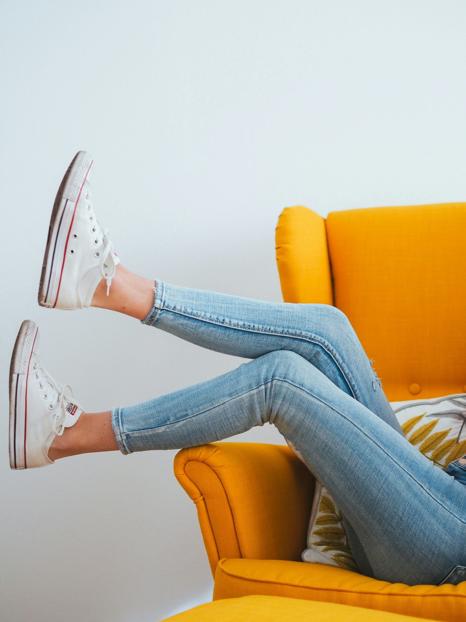 woman wearing skinny jeans and sneakers sitting in a yellow chair