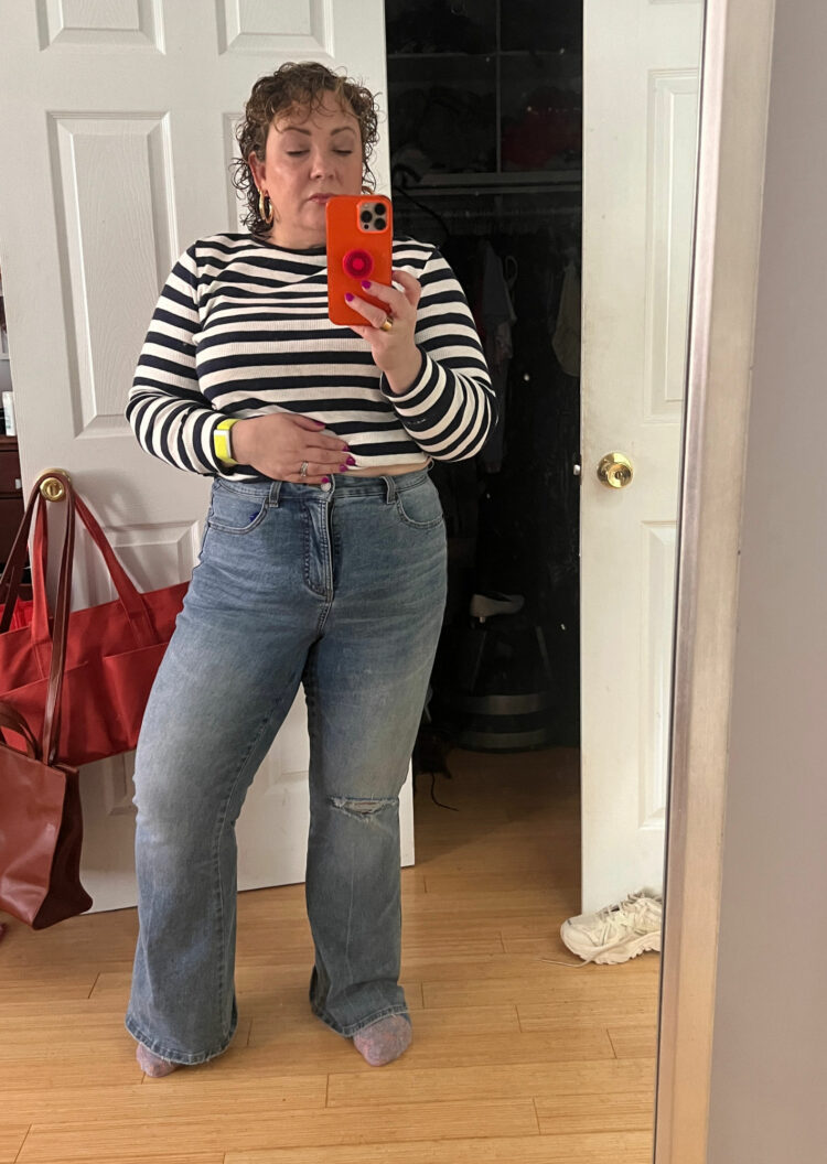 Woman in a navy and white stripe Breton top and a faded pair of the Universal Standard Farrah flared jeans