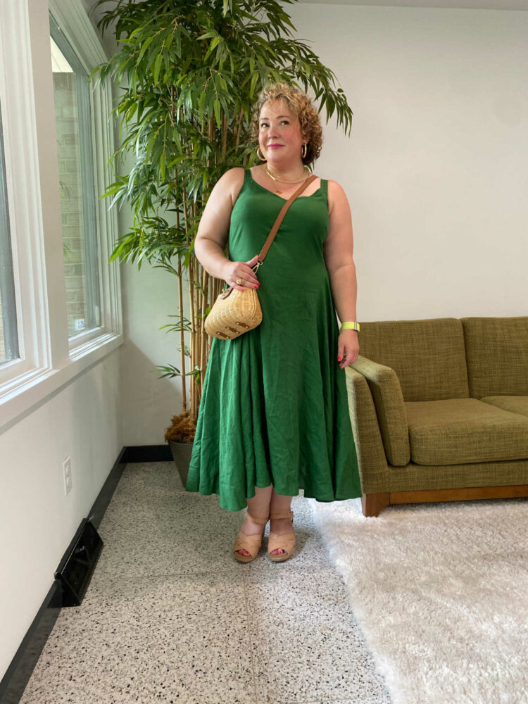 Alison wearing the Universal Standard Sunshower dress in green with brown sandals and a wicker crossbody bag