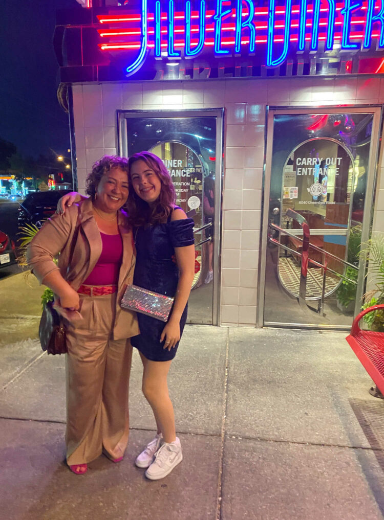 Alison and her daughter in front of a diner. Alison is wearing a tan satin pantsuit with a berry colored tank and berry suede strappy heeled sandals.