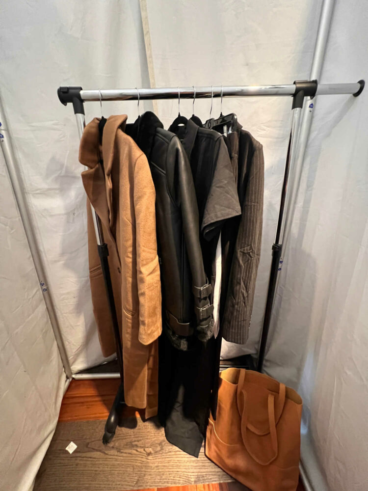 a rolling rack inside a fabric fitting room at a Universal Standard trunk show. The rolling rack has two coats, a jumpsuit, a pair of pants and matching blazer