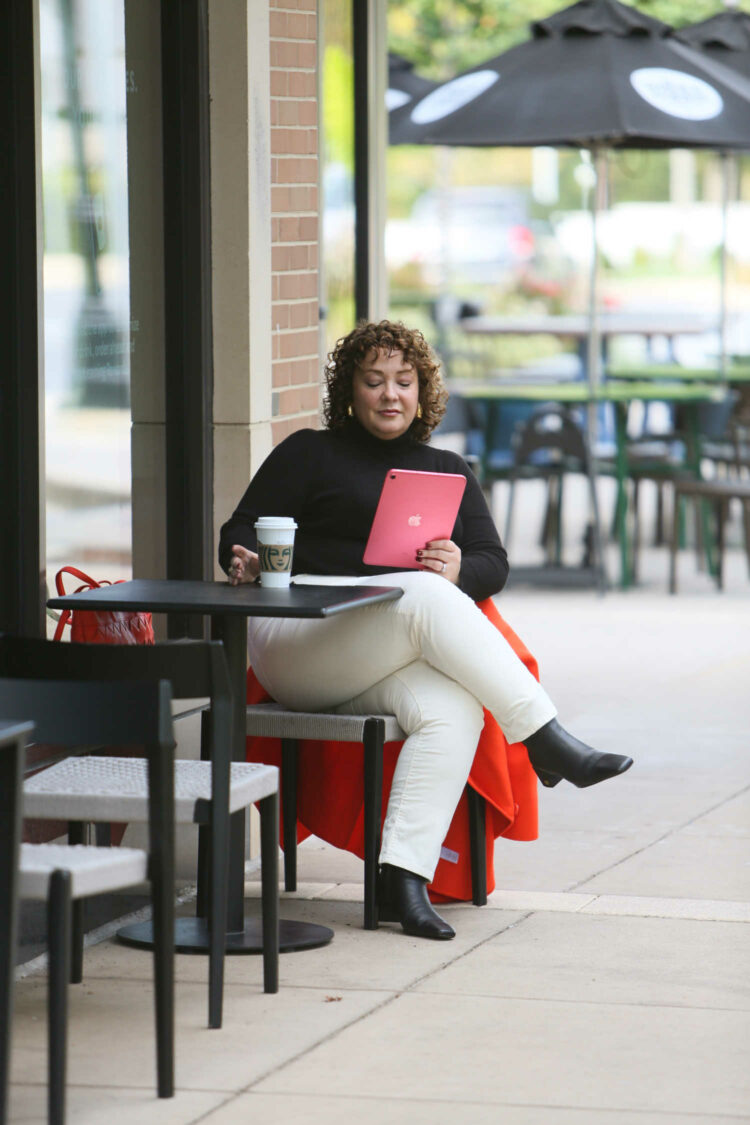 Alison Gary of Wardrobe Oxygen wearing ivory corduroy pants from Talbots as she sits at a coffee shop drinking a latte and reading from her iPad