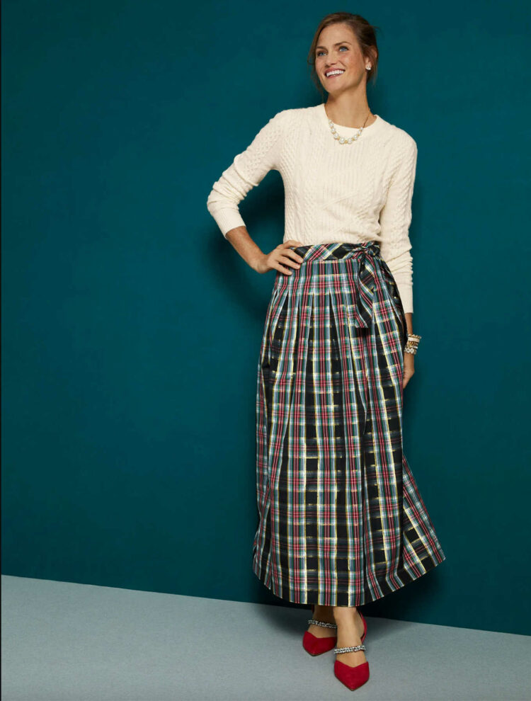 A photo from the Talbots website of a model in a cream cableknit sweater and a metallic plaid ball skirt