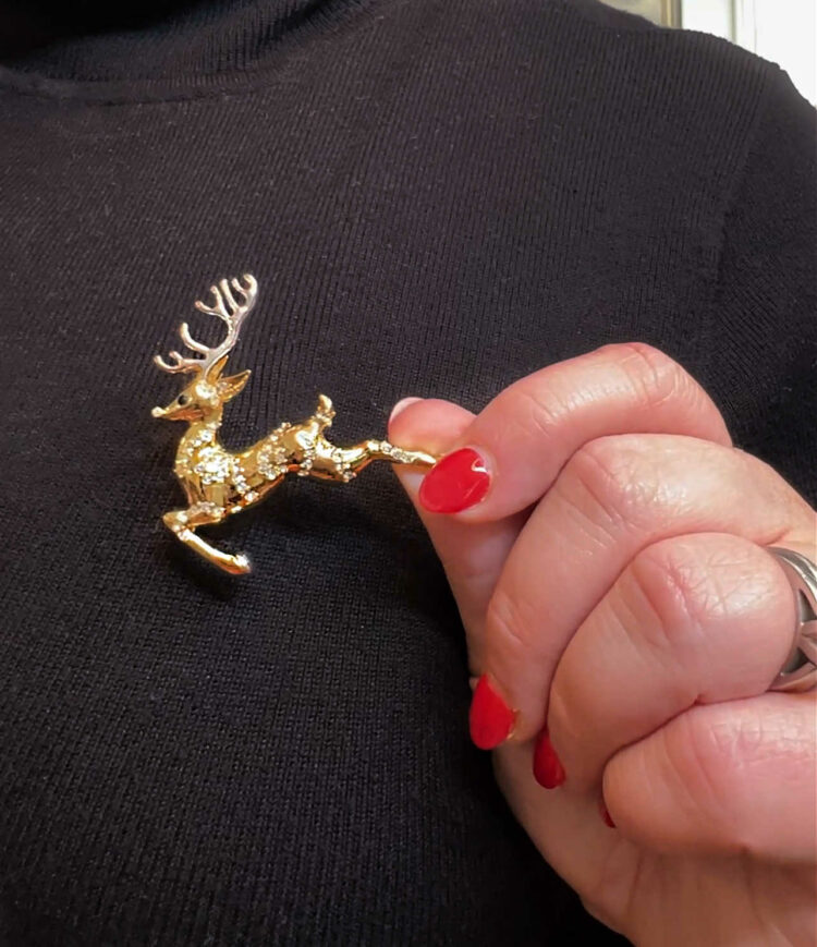 a gold brooch shaped like a reindeer with silver horns and crystals embedded into the body