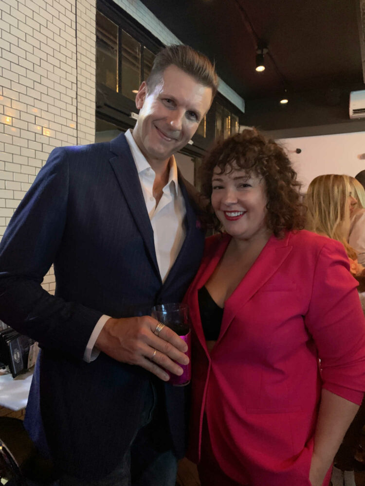 A man and woman in suiting at a bar. The man is in a navy chalkstripe suit from Banana Republic with a white shirt with the collar open. The woman is in a hot pink Banana Republic pantsuit.