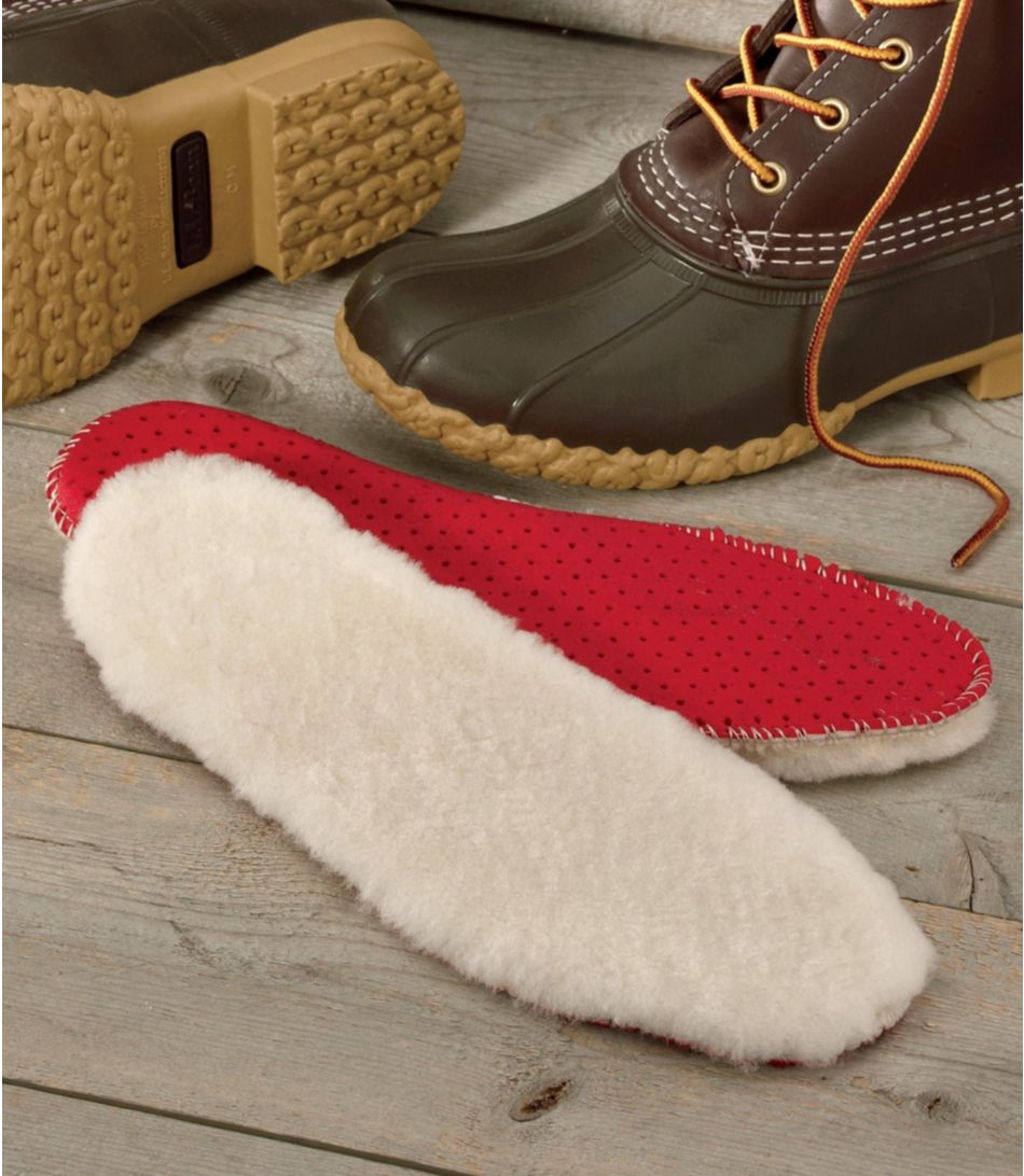 two shearling shoe insoles with red ventilated bottoms on the floor next to a pair of L.L. Bean duck boots
