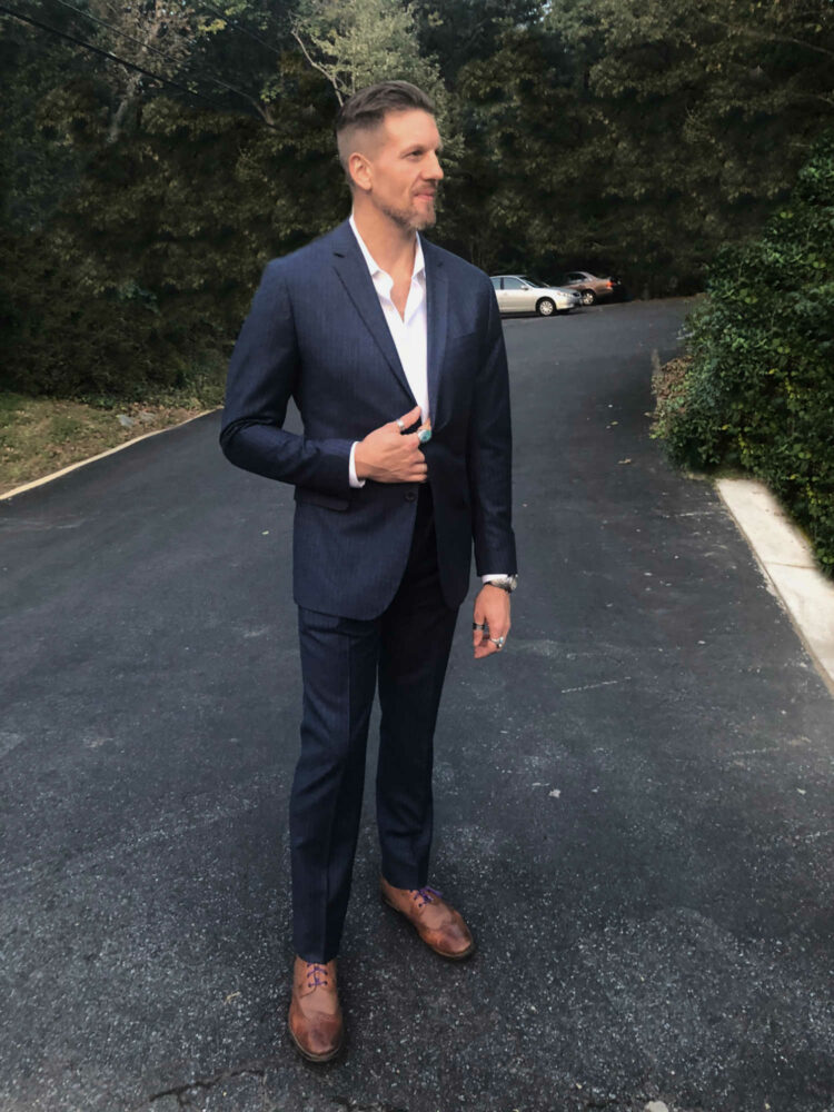 man in a navy suit and white shirt standing in a road