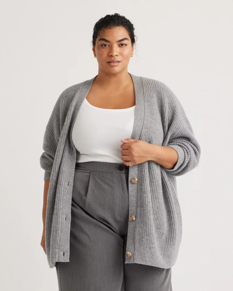 a plus size model wearing the Quince Mongolian Cashmere Oversized Boyfriend Cardigan Sweater in gray over a white tank and gray pleated trousers