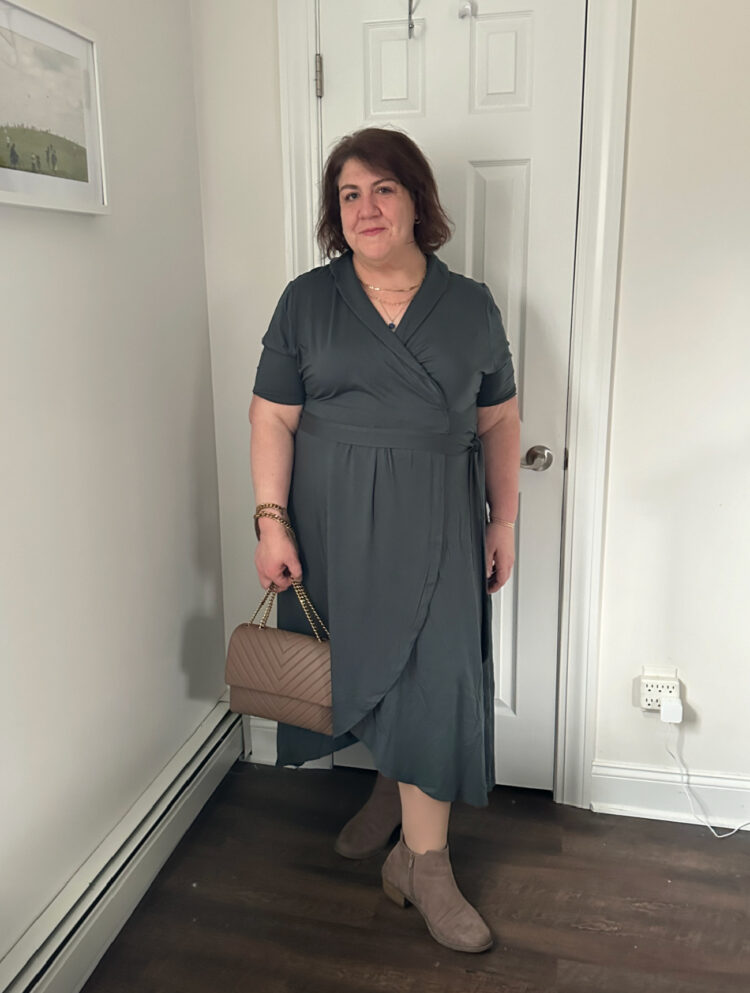 woman in a teal short sleeve tencel wrap dress from Quince. She is wearing taupe ankle boots and holding a taupe quilted leather handbag, which is also from Quince.