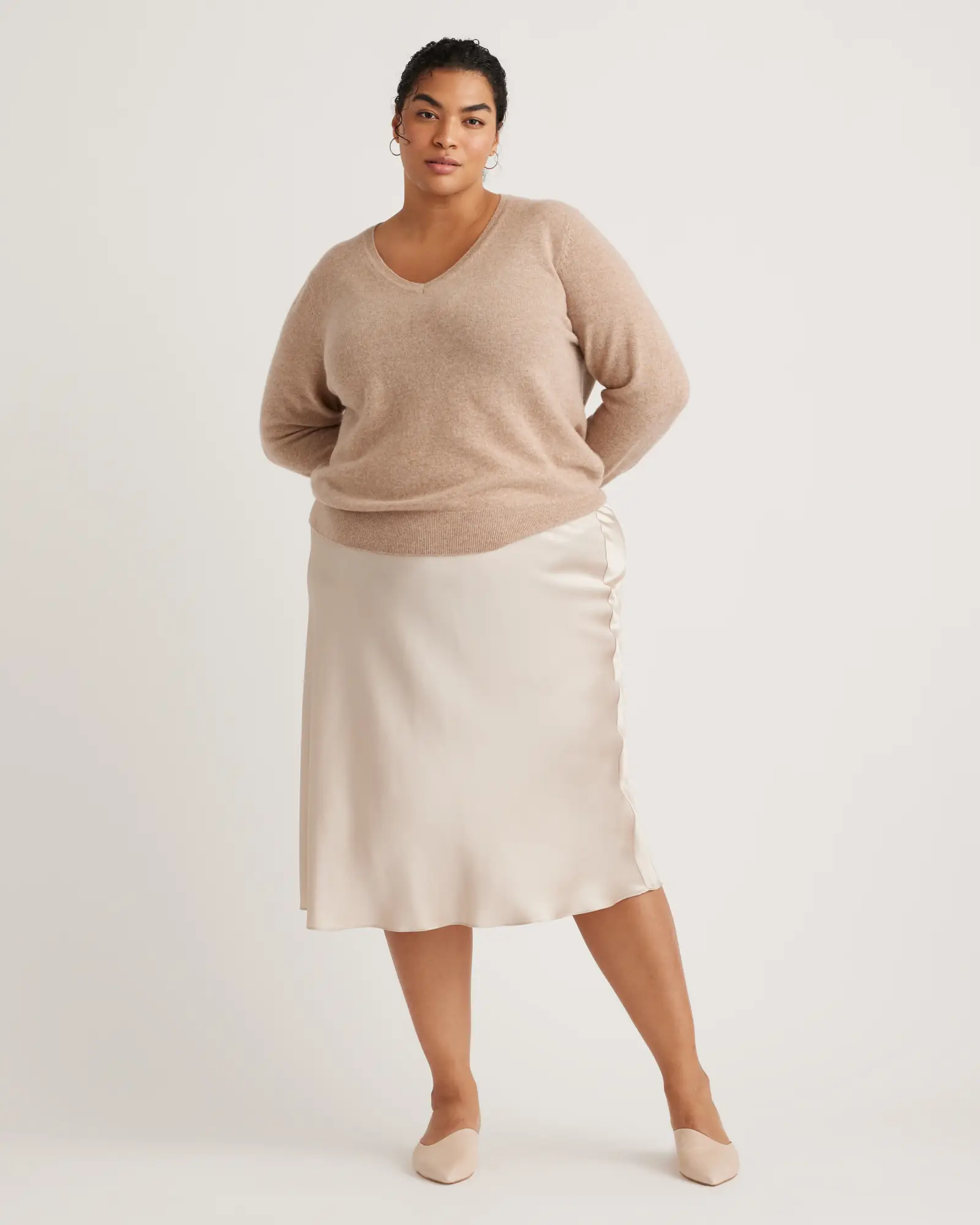 model wearing the Quince plus size mongolian v-neck sweater in camel with the champagne colored Quince washable silk skirt.
