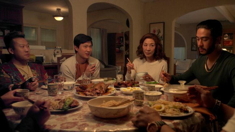 A scene from the Netflix series, The Brothers Sun where Mama Sun, Charles, Bruce, and KT are sitting around the dinner table eating and talking.