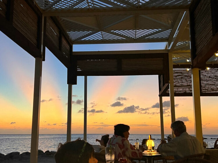 a view of a sunset from a table under an awning in front of a beach