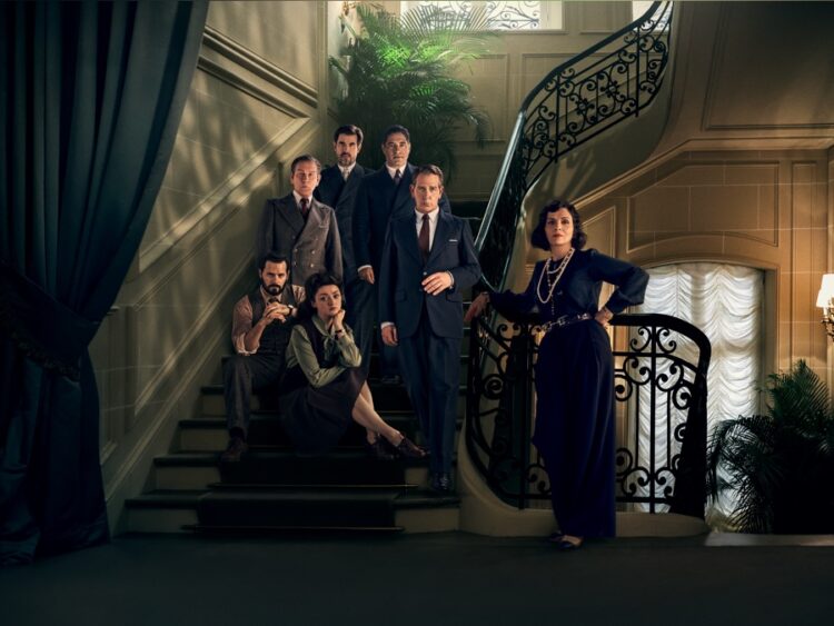 the stars of the apple tv series the new look sitting on a staircase