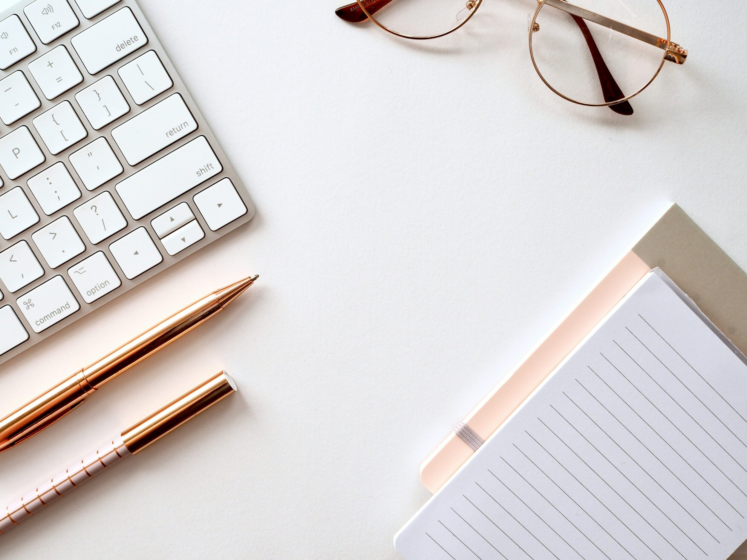 a desk featuring reading glasses, a laptop for blogging, a journal, and several decorative pens