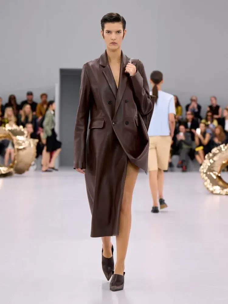 A model walking the runway in the Loewe Spring Summer 2024 show wearing a brown leather calf-length double breasted coat