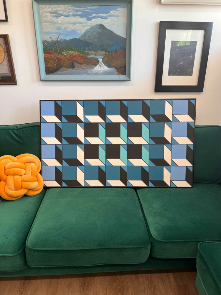 a black, white, and blue graphic painting sitting on Alison's green velvet sofa
