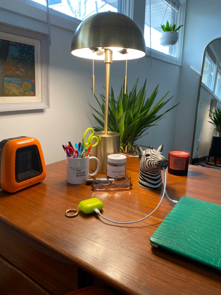 top of my desk with an orange heater, brass lamp, and a zebra pitcher as a cord catcher