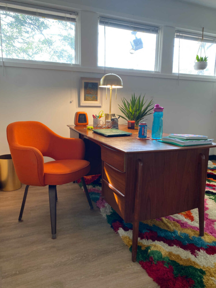 orange wool chair with wood legs behind a mid century modern office desk