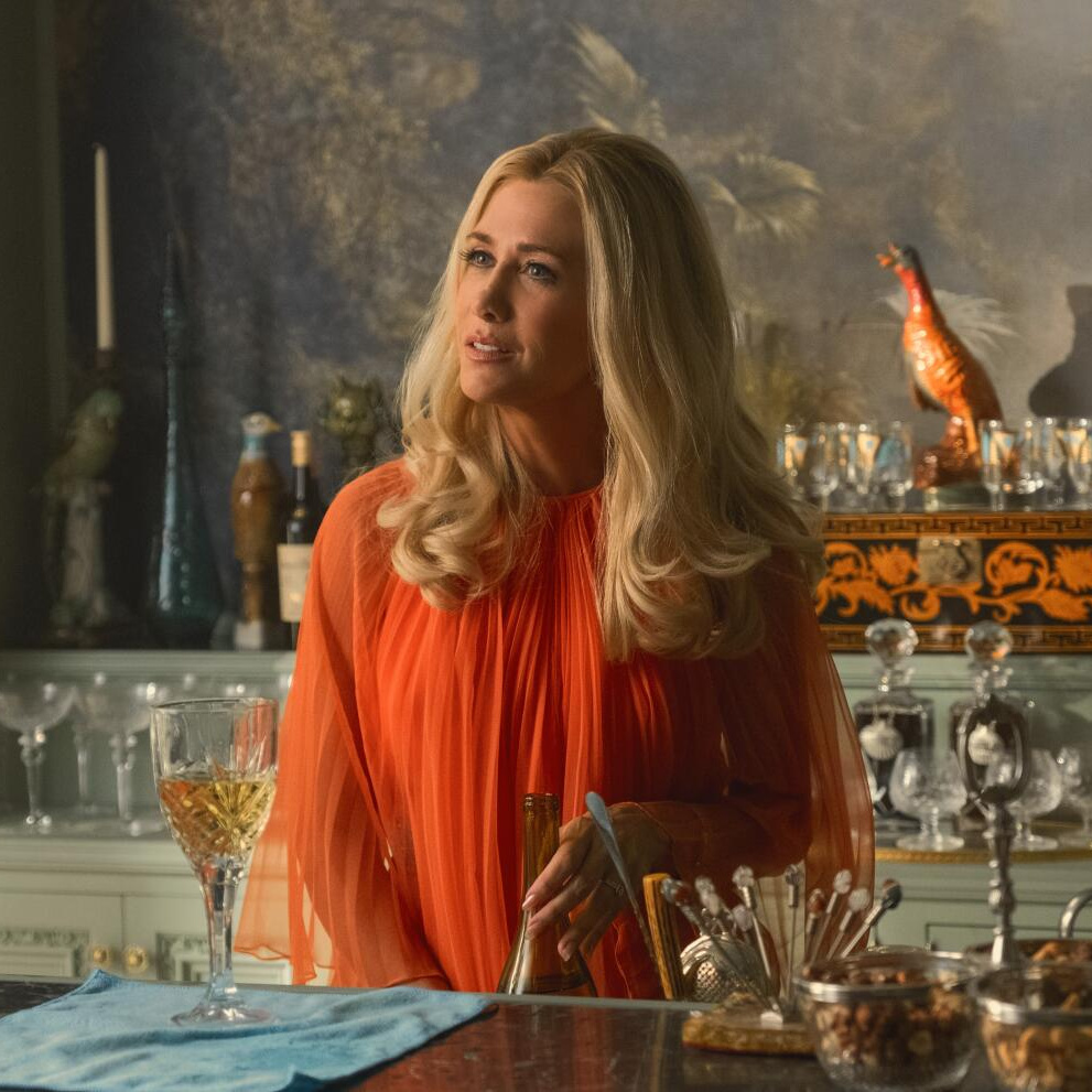 Kristin Wiig in Palm Royale, wearing an orange chiffon caftan looking thoughtful