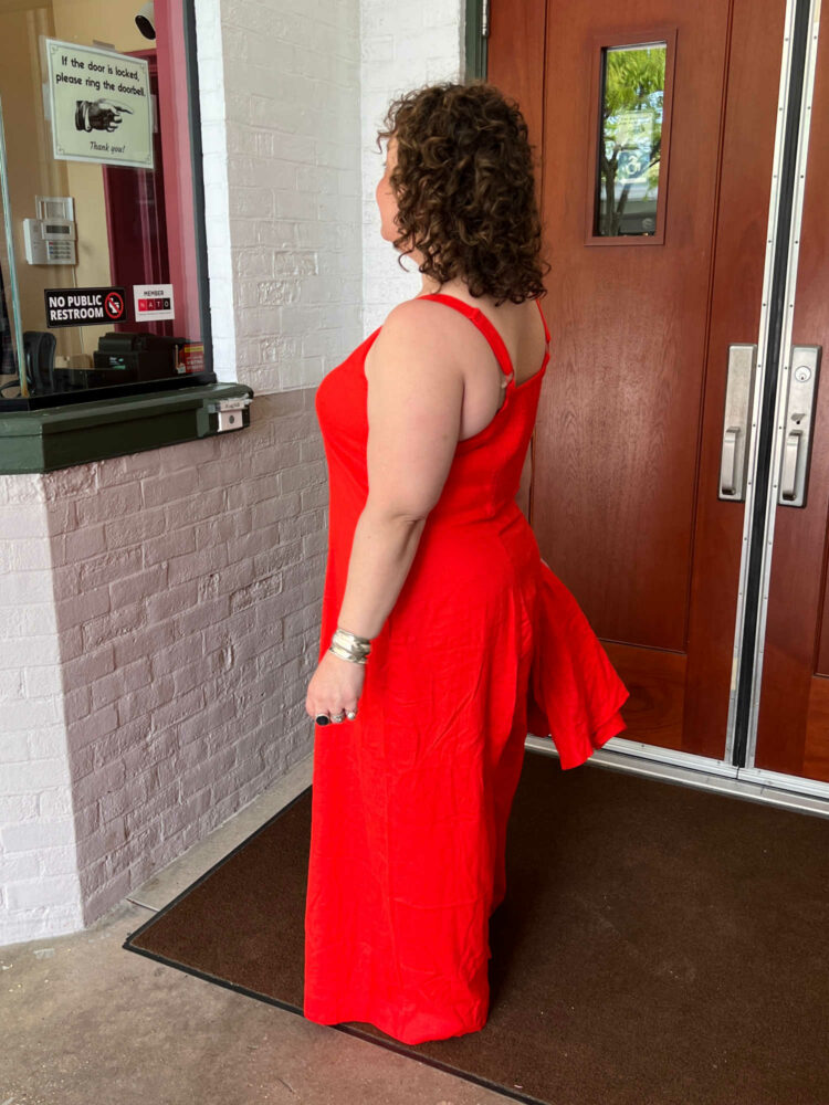 Alison in profile, showing the back of the Universal Standard linen Promenade jumpsuit, which has 1" wide adjustable straps and an elasticized smocked back