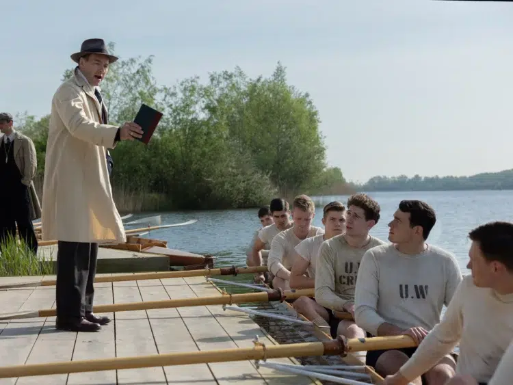the boys in the boat cast; the rowers in the boat and the coach on the pier talking to them