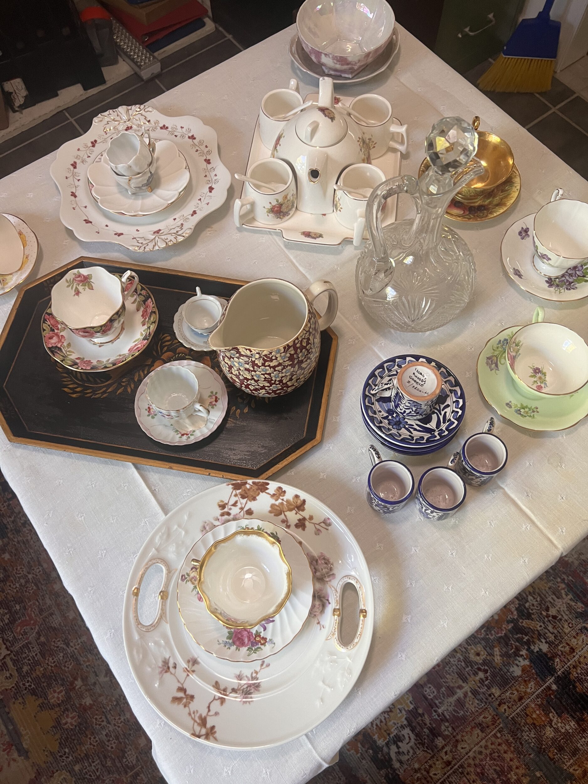 a picture of a table at an state sale covered with a tablecloth, holding various pieces of china and crystal