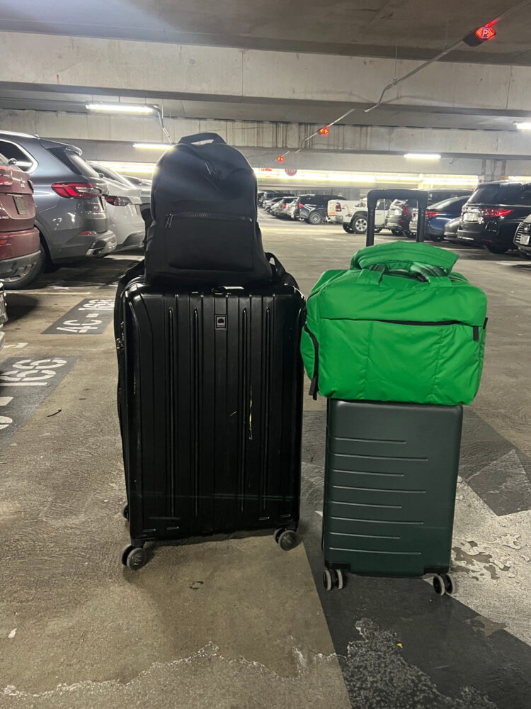 Quince Suitcase Review Suitcases, including the Quince small expandable suitcase, in an airport parking lot