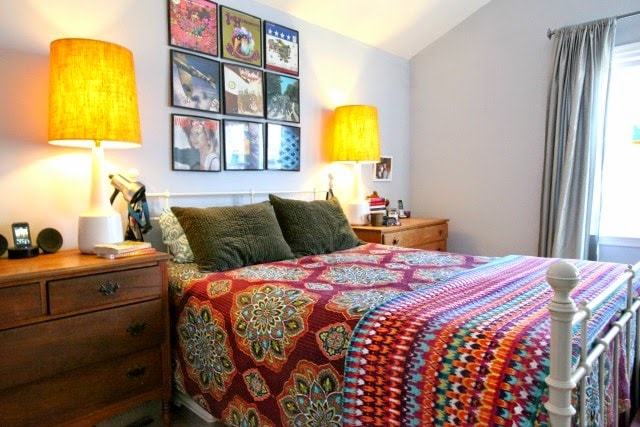 a bedroom with a bed made with colorful quilts and printed sheets