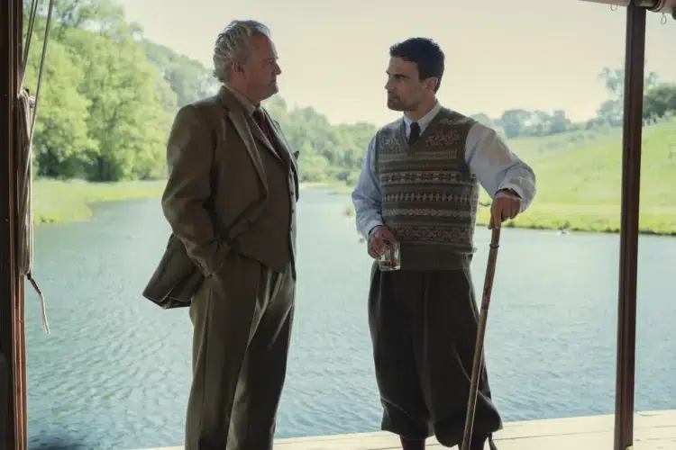 Weekend Reads for the End of September 4 "Two men in aristocratic clothing talk by a riverbank; one holds a drink, the other a walking stick. They stand under a shaded structure with green trees and calm water visible in the background on a sunny day."
