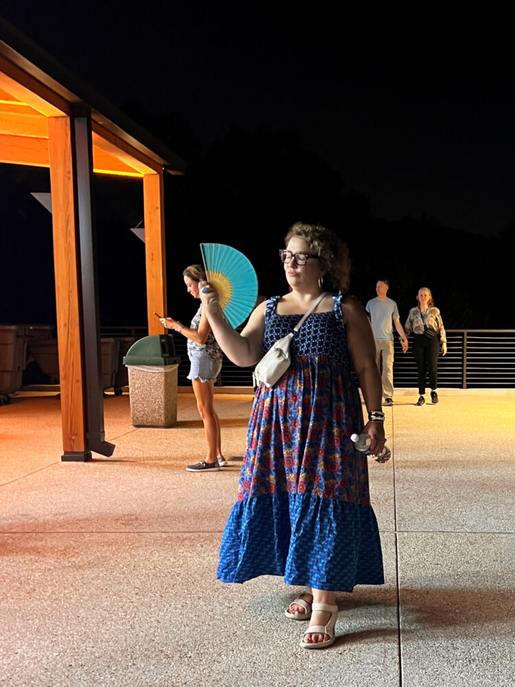 Woman in a printfresh maxi sundress holding a folding fan walking through the grounds at Wolf Trap